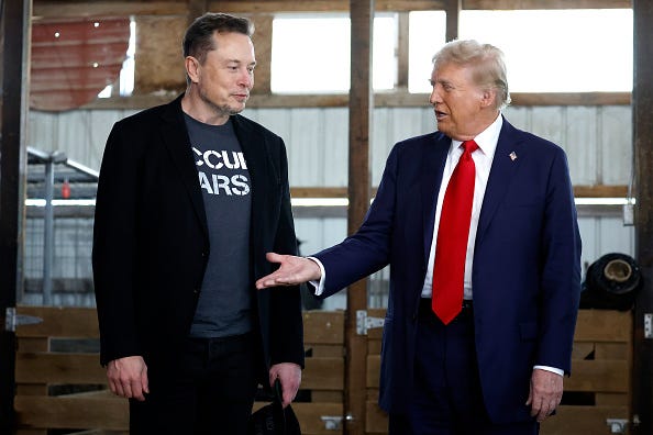 Republican presidential nominee, former President Donald Trump offers his hand to Elon Musk back stage during a campaign rally at the Butler Farm Show grounds on October 05, 2024 in Butler, Pennsylvania. 