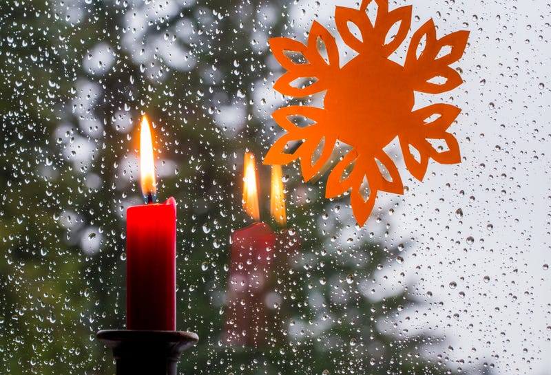 candle and paper snowflake on rainy window 
