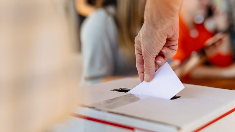 A hand drops a ballot into a box.