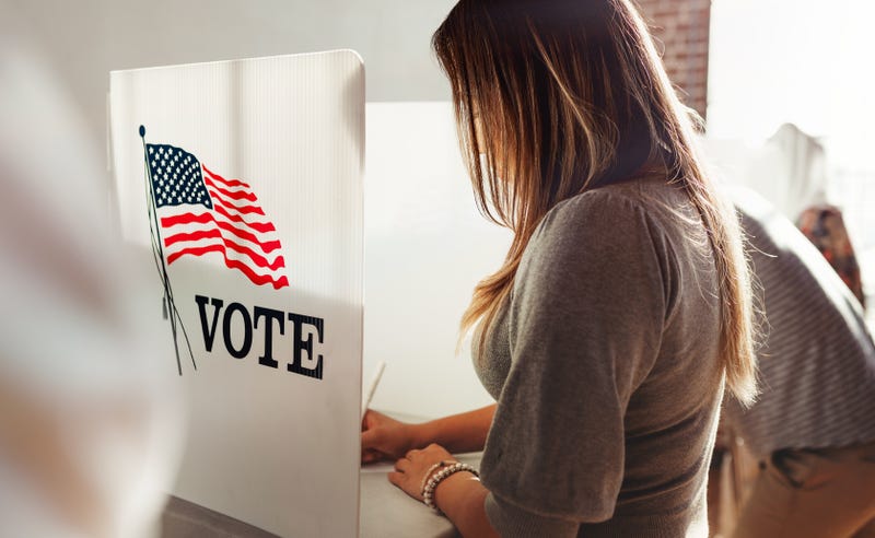 Woman stands in a voter booth, filling out a ballot