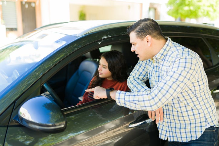 father instructing his teenage daughter on driving while pointing out something inside the car