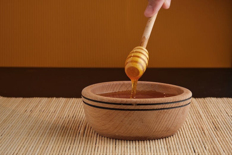 A honey stick dipper being dipped into a wooden bowl