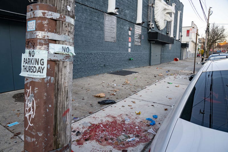 Blood is visible on the sidewalk the morning after four gunmen opened fire at a crowd of about 15 people waiting outside the the Amazura Concert Hall in Jamaica, Queens.