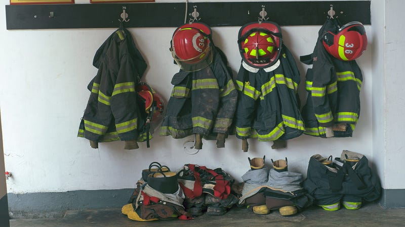 Firefighter uniforms and helmets hanging on a wall in a fire station - stock photo