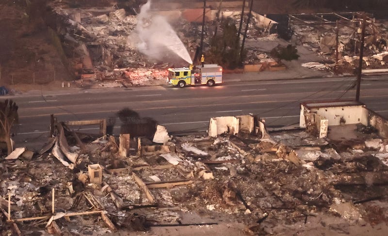 An aerial view of firefighters spraying water on a destroyed property as the Palisades Fire continues to burn on January 09, 2025 in Malibu, California.