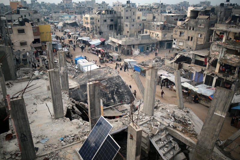 People walk past stalls selling goods amid the rubble of buildings destroyed during previous Israeli strikes, in Khan Yunis in the southern Gaza Strip.