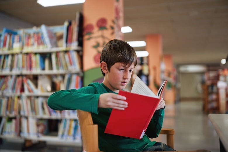 Boy reading a red book in a library