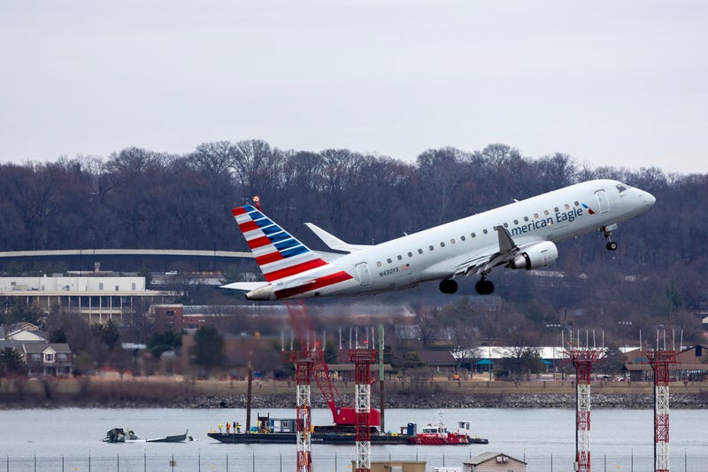 ARLINGTON, VIRGINIA - FEBRUARY 02: An American Eagle Embraer 170 jet takes off from Reagan National Airport as a crane moves in to place on the Potomac River for recovery efforts on February 02, 2025 in Arlington, Virginia. An American Airlines flight from Wichita, Kansas collided midair with a military Black Hawk helicopter while on approach to Ronald Reagan Washington National Airport on January 29, 2025 outside of Washington, DC. According to reports, there were no survivors among the 67 people onboard both aircraft. (Photo by Tasos Katopodis/Getty Images)