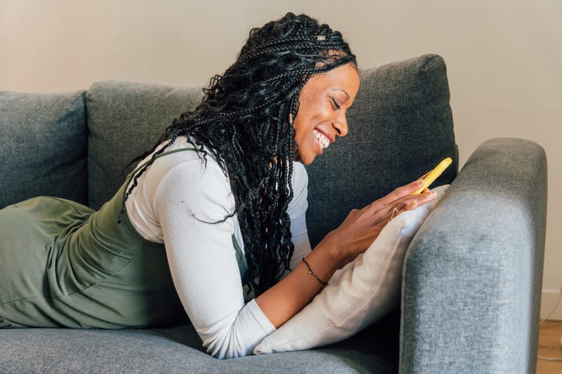 Woman lays on couch and smiles as she reads a text on her phone