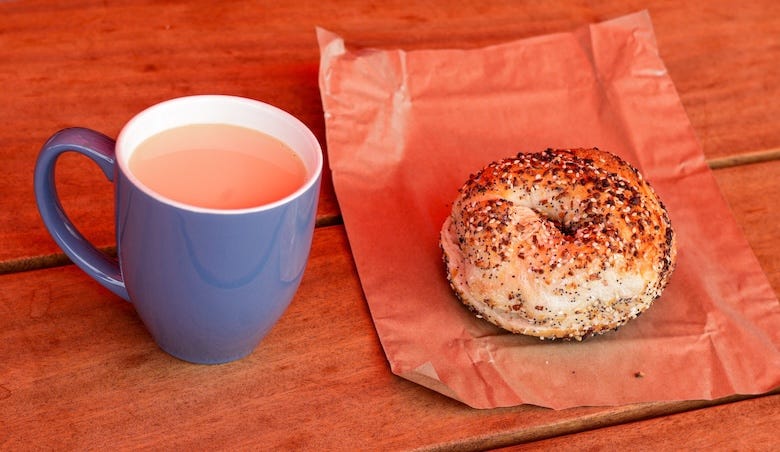 Cup of coffee and an everything bagel on a wooden table