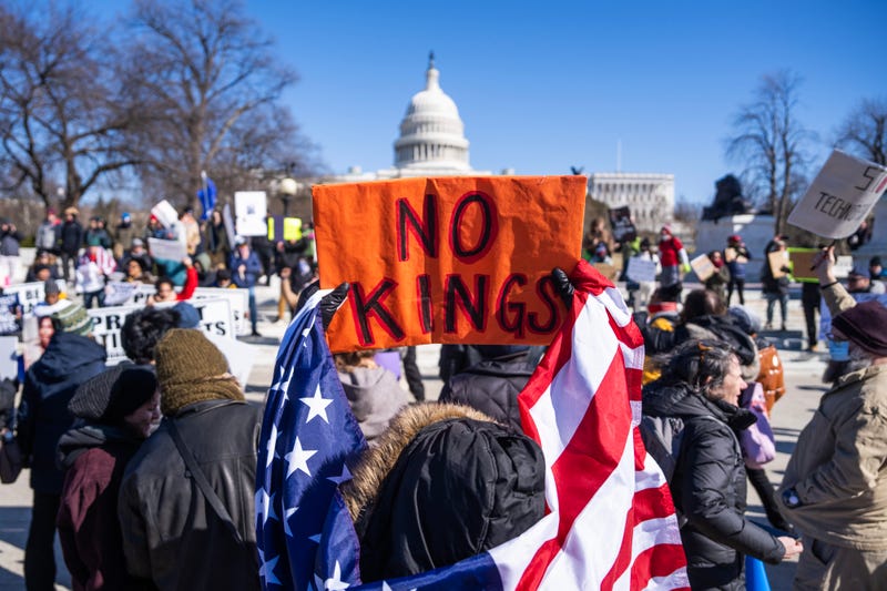 Demonstrators hold signs during the No Kings Day protest to oppose the Trump administration's policies, including efforts to cut the federal workforce, at the Capitol Reflection Pool on Presidents Day, Feb. 17, 2025. 