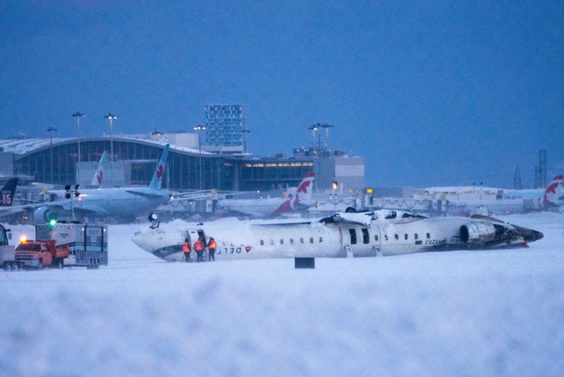 Airport workers survey the site of a Delta Air Lines plane crash that injured at least 18 passengers at Toronto Pearson International Airport on February 18, 2025 in Toronto, Canada. The jet, coming in from Minneapolis, attempted to land amid strong winds and snow, leading to it crashing and landing upside down on the tarmac the day before. 