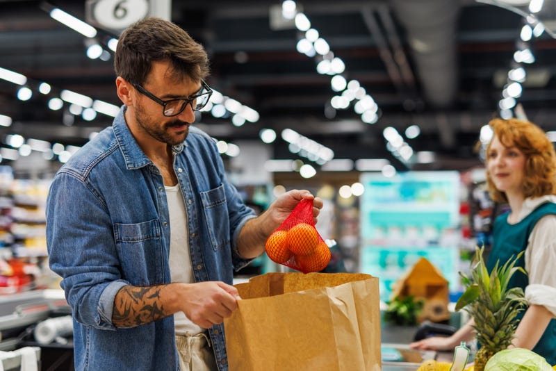 Man placing oranges inside a paper grocery bag at the store.