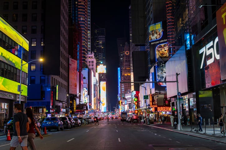 A lively crowd fills the streets of Times Square, surrounded by bright, colorful billboards that light up the night sky, creating an energetic atmosphere.