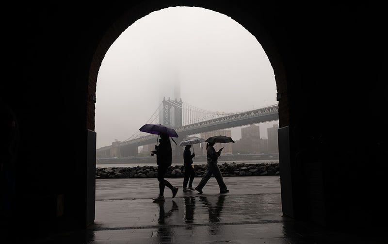 People walk in the rain across from a fog-covered Manhattan skyline on May 6, 2025 in New York City.