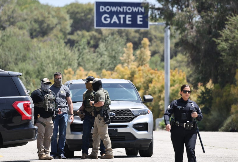An LAPD officer walks near masked federal agents staged outside a gate of Dodger Stadium on June 19, 2025 in Los Angeles,