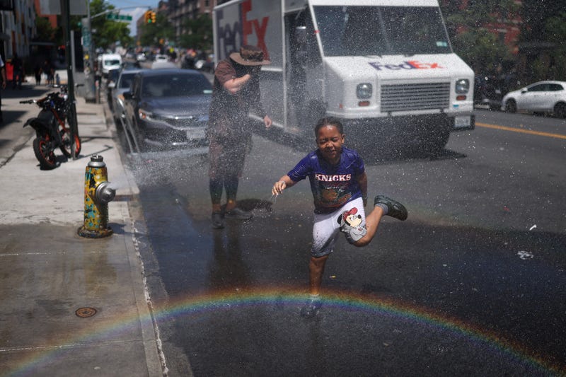 A boy and a delivery driver cool off at a fire hydrant in Washington Heights