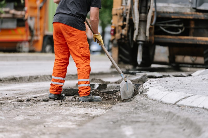 Construction worker repairs road surface with shovel and machinery