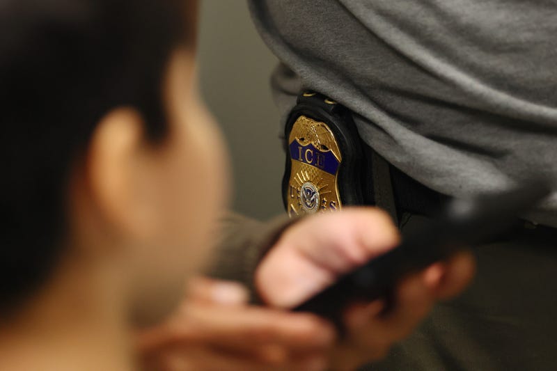 A child looks at the badge of an Immigration and Customs Enforcement (ICE) agent as his family is helped in the halls of immigration court at the Jacob K. Javitz Federal Building on July 23, 2025, in New York City.