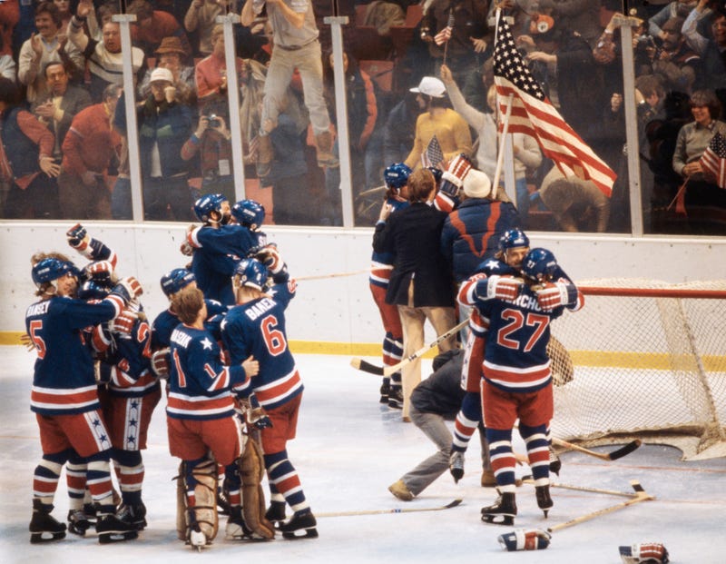Players from the United States Ice Hockey team celebrate and wave the Stars and Stripes flag after defeating Team Finland to win the gold medal during the Men's Ice Hockey Final game on 24th February 1980 during the XIII Olympic Winter Games at the Olympic Fieldhouse Olympic Arena in Lake Placid, New York, United States. 