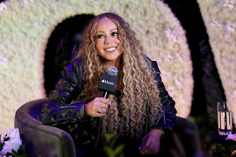 Mariah Carey with a microphone sitting on stage