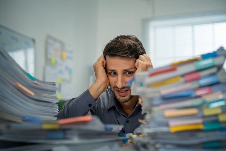 Man staring at piles of papers on his office desk