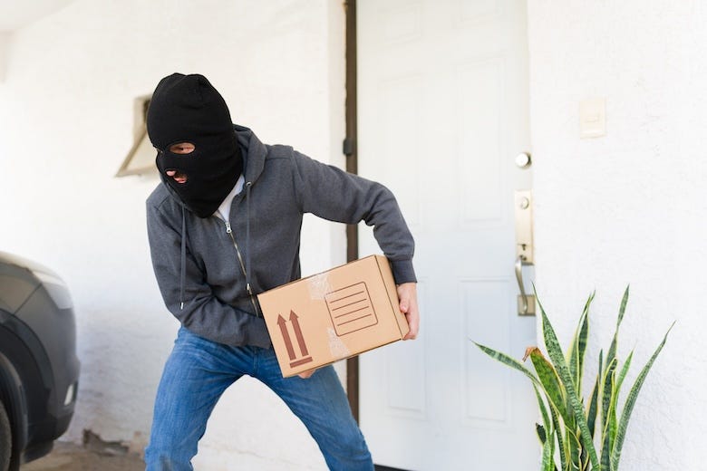 Masked thief stealing a package from a porch