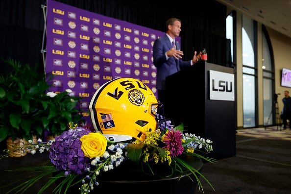 LSU head coach Lane Kiffin in the background with an LSU helmet in the foreground 