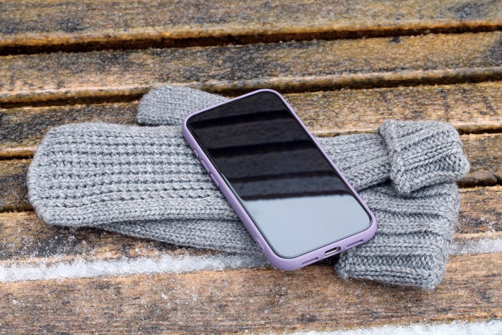 Smartphone with purple case resting on grey knitted mittens during winter in outdoor setting