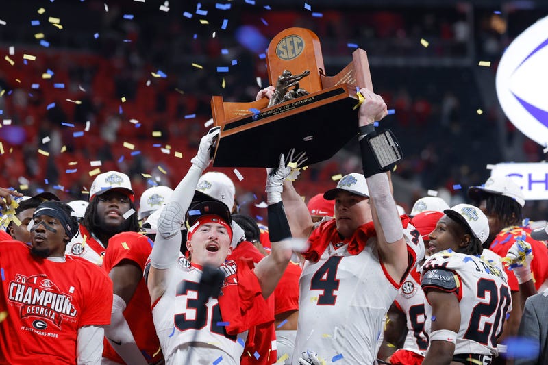 Cash Jones #32 and Oscar Delp #4 of the Georgia Bulldogs raise the 2025 SEC Championship trophy after defeating the Alabama Crimson Tide 28-7 at Mercedes-Benz Stadium.