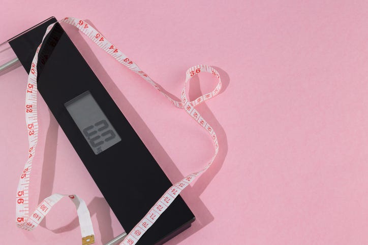 Bathroom scale with a measuring tape placed on top on a pastel pink background with space for text. Weight control concept, wellness, healthy diet, and balanced lifestyle