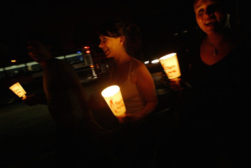 In the dark of a night without power, people in New York walk down the street holding candles. 