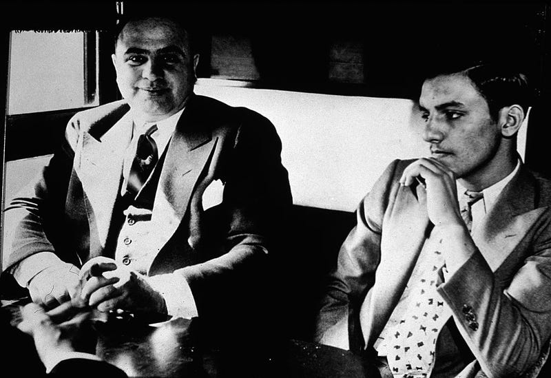 American gangster Al Capone ('Scarface') (1899 - 1947) sits in a train compartment with an unidentifed associate (R) during his transport to prison to serve a sentance for tax evasion, October 1931. (Photo by Hulton Archive/Getty Images)