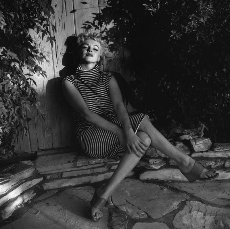 American actress Marilyn Monroe (1926 - 1962) sits in shadow against a garden fence, 1954.