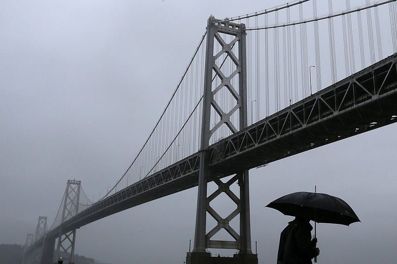 A pedestrian walks in the rain next to the San Francisco-Oakland Bay Bridge on December 11, 2014 in San Francisco, California.