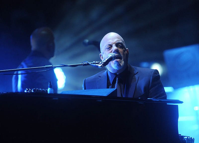 Billy Joel singing on stage while seated at a piano