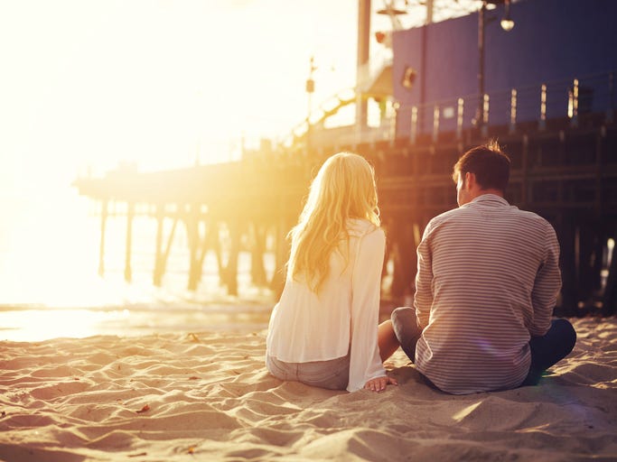 romantic couple sitting together by the beach with sunset