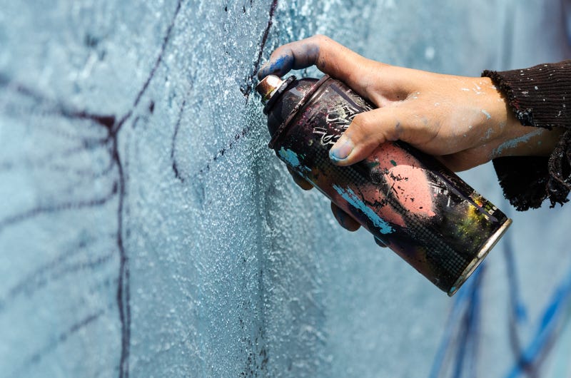 Person spray painting graffiti on brick wall