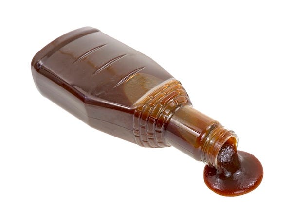 Bottle of barbecue sauce spilling against a white background