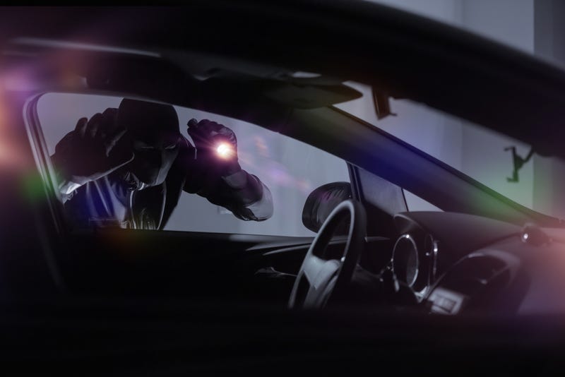 robber in ski mask looks through car window with flashlight