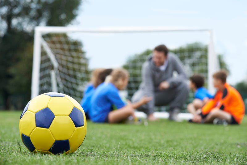 Coach and team discussing soccer tactics with ball in foreground.