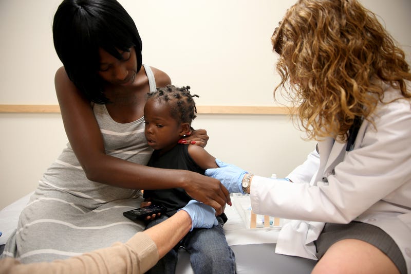 A pediatrician administers a measles vaccine to a child while their mother holds them.