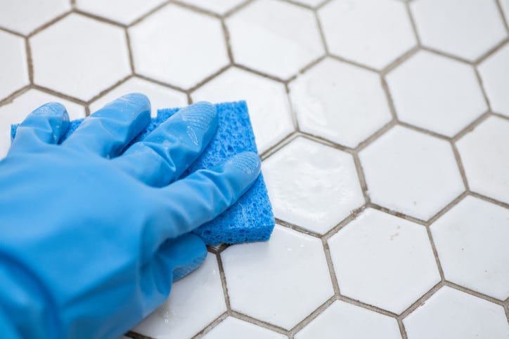 gloved hand cleaning grout with a sponge