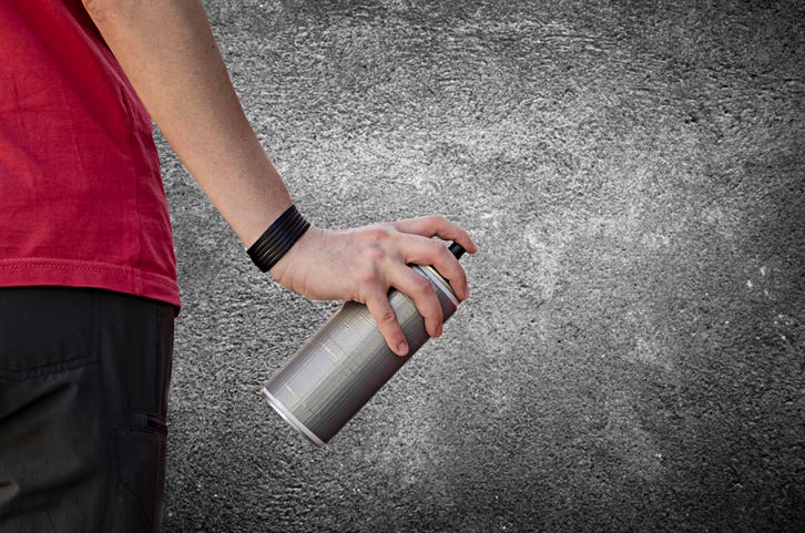 Person holding a can of spray paint in front of a wall, getting ready to paint something.