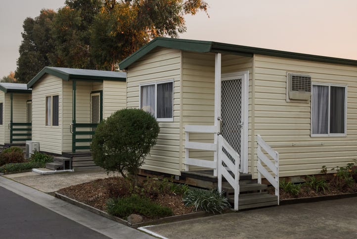 A row of mobile homes including one with a white fence up the porch stairs a bush out front.