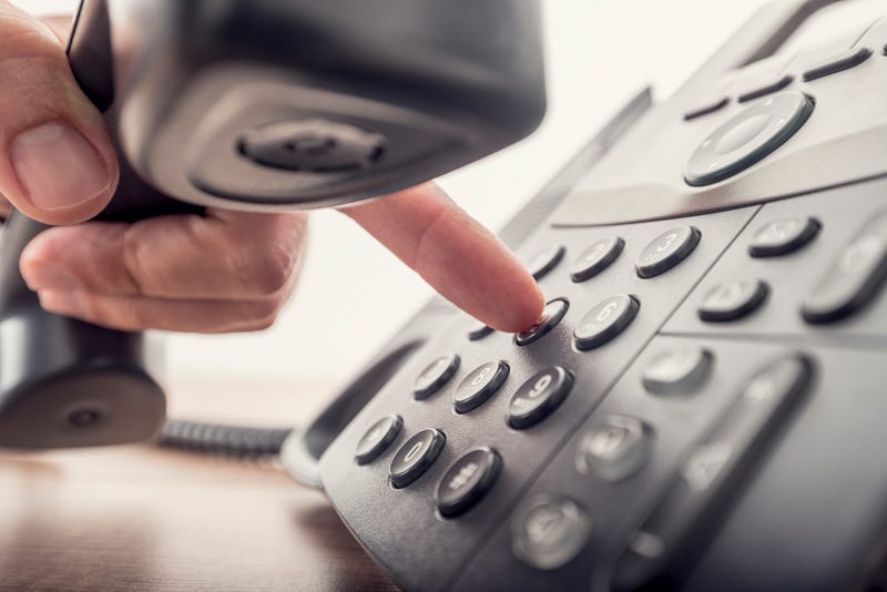 Closeup of male hand holding telephone receiver while dialing a telephone number to make a call using a black landline phone.