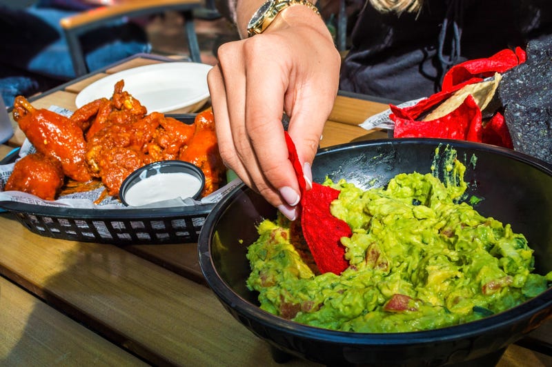 A girl dips into the guacamole with chips along with buffalo wings on the side as appetizers.