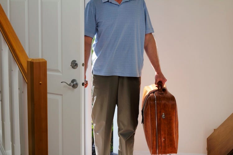 Man walking into home carrying suitcase