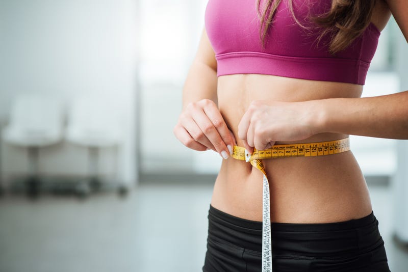Slim young woman measuring her waist with a tape measure