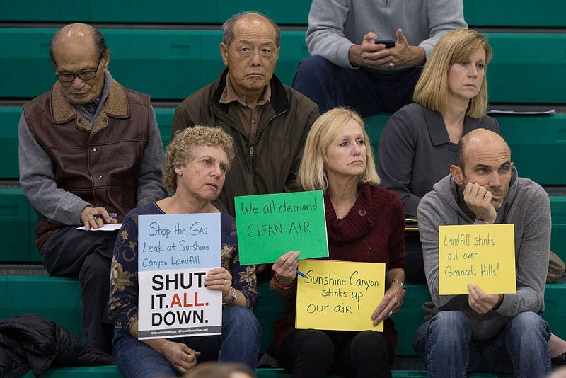 People hold signs while attending a public hearing before the South Coast Air Quality Management District (AQMD) regarding a proposed stipulated abatement order to stop a nearby massive natural gas leak, on January 16, 2016 in Granada Hills, near Porter Ranch, California.